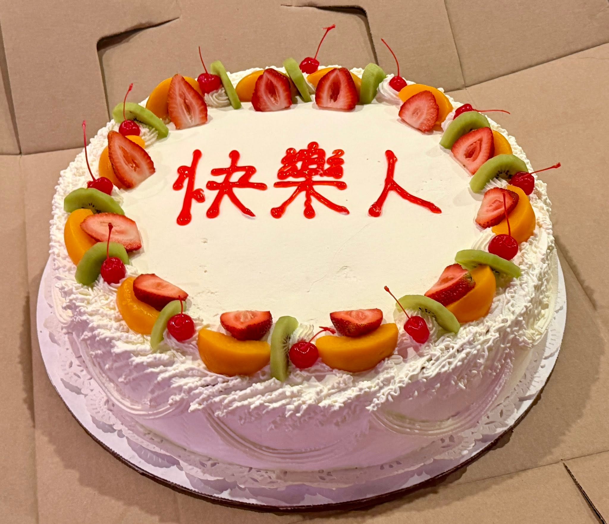 A decorated cake with fruit and the Chinese characters 快樂人